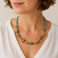 KI-generierte Frau in weißer Bluse mit einer türkis-patina-farbenen Perlenkette und altgoldfarbenen Musterperlen als Stylingbeispiel.