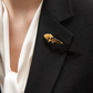 KI-generierte Frau trägt eine goldfarbene Brosche mit Rosenmotiv und braunen Tigerauge-Splittern am Revers eines schwarzen Blazers über einer weißen Bluse.