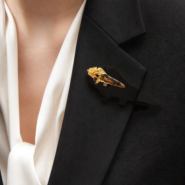 KI-generierte Frau trägt eine goldfarbene Brosche mit Rosenmotiv und braunen Tigerauge-Splittern am Revers eines schwarzen Blazers über einer weißen Bluse.