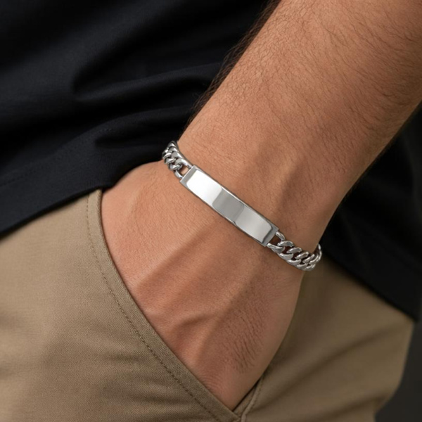 KI-generierte Person trägt ein silberfarbenes Panzerketten-Armband mit blanker Schildplatte am Handgelenk, kombiniert mit schwarzem Oberteil und beiger Hose.