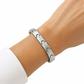 KI-generierte Frau trägt ein silberfarbenes Edelstahl-Gliederarmband mit geschwungenen Übergängen am Handgelenk zu einem weißen Oberteil.
