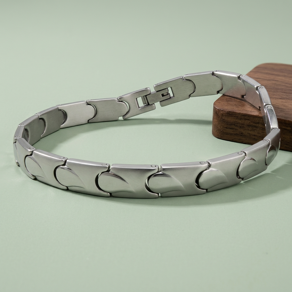 Silberfarbenes Edelstahl-Gliederarmband mit geschwungenen Übergängen auf salbeigrünem Untergrund, seitlich auf einem dunklen Holzstück abgestützt.