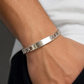 KI-generierter Mann trägt ein silberfarbenes Edelstahl-Schildband-Armband mit Flachpanzerkette und blanker Gravurplatte zu einem hellen Oberteil.