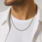 KI-generierter Mann trägt eine silberfarbene Edelstahl-Panzerkette ohne Anhänger zu einem weißen T-Shirt und offenem weißen Hemd.