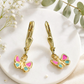Schmetterlings-Ohrhänger aus 9 Karat Gold mit pink-hellblauen Flügeln vor dekorativem Hintergrund