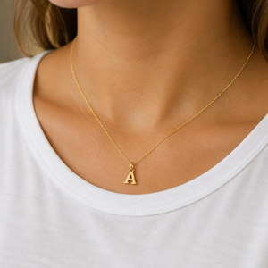 KI-generierte Frau im weißen Oberteil trägt einen kleinen goldenen A-Anhänger an einer feinen Kette als Stylingbeispiel.