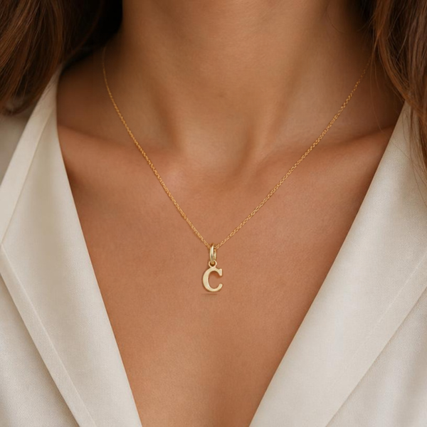 KI-generierte Frau trägt einen goldfarbenen C-Anhänger an einer feinen Kette zu einer weißen Bluse.