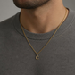 KI-generierter Mann trägt einen goldfarbenen C-Anhänger an einer Kette zu einem grauen Pullover.