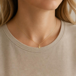 KI-generierte Frau trägt einen goldfarbenen F-Anhänger an einer feinen Kette.
