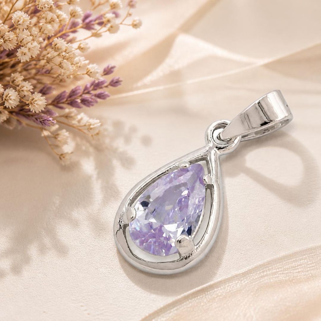 Tropfen-Anhänger aus Silber 925 mit lavendelfarbenem Zirkonia auf hellem Satin neben zarten Blüten