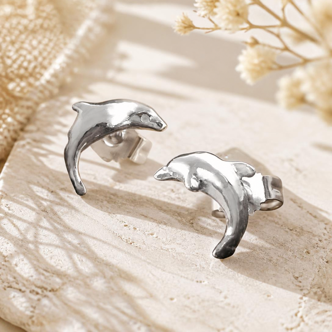 Glänzende Delfin-Ohrstecker aus Silber 925 auf hellem Stein mit dezenter weißer Blütendekoration