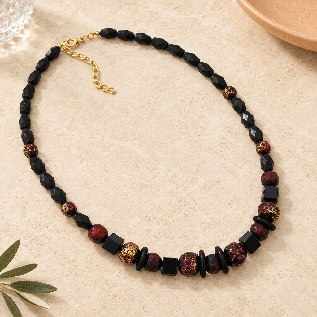 Schwarze Perlenkette mit rot-goldfarbenen Akzenten auf hellem Stein mit apricotfarbener Keramik, strukturiertem Glas und Olivenzweig.