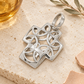Filigraner Weißgold-Kreuzanhänger auf hellem Travertin mit bernsteinfarbenem Glas, Olivenzweig und apricotfarbenen Keramikstücken.
