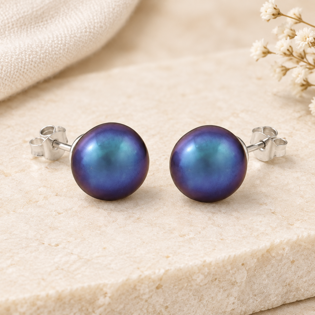 Blau-violett schimmernde Perlen-Ohrstecker aus Silber 925 auf hellem Naturstein mit cremefarbenem Leinen und weißen Blüten